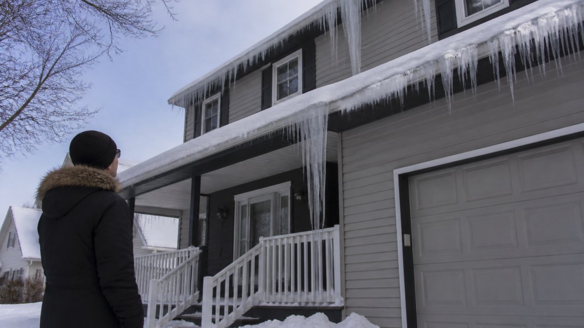 Homeowner looking up at dangerous icicles on a house roof caused by ice damming